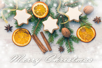 Christmas decoration over white wood wood background. Top view of homemade butter nuts star shaped cookies with icing, pine, orange slices,cinnamon, anise, walnuts and white ribbon. 