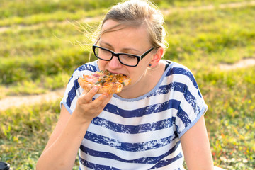 Young woman eating pizza on meadow, relax in nature
