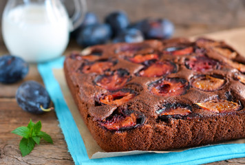 Chocolate cake with plums on a dark background with milk 