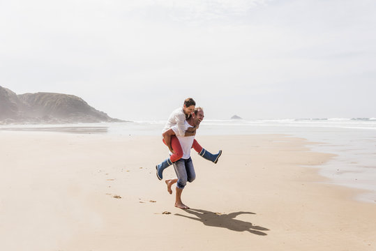 Happy mature man carrying wife piggyback on the beach