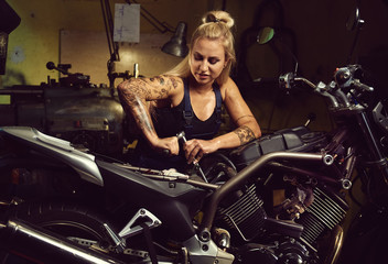 Obraz na płótnie Canvas Blond woman mechanic repairing a motorcycle in a workshop