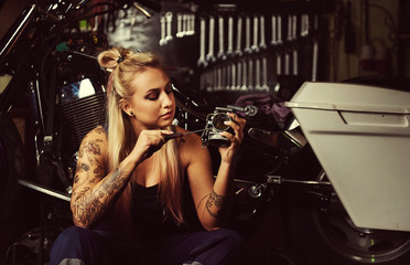 Fototapeta na wymiar Blond woman mechanic repairing a motorcycle in a workshop