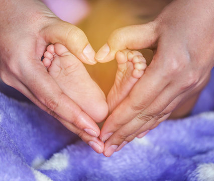 Newborn baby feet in the mother hands heart shaped 