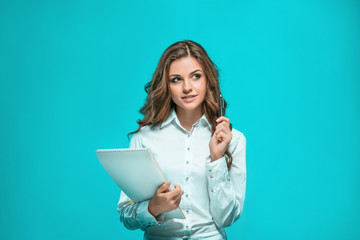 The smiling young business woman with pen and tablet for notes on blue background