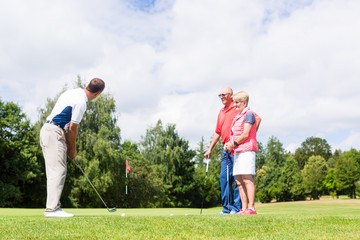 Golf pro practicing the sport with senior woman and man