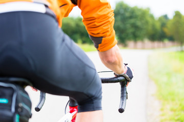 Mann auf Fahrrad oder Rennrad macht Sport und fährt auf Landstraße, Blick von hinten über Schulter