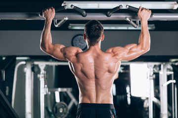 Naklejka na ściany i meble Athlete muscular fitness male model pulling up on horizontal bar in a gym