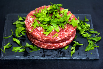 Raw hamburgers with parsley on a stone slate