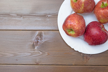 Four fresh red apples in white plate on wooden background