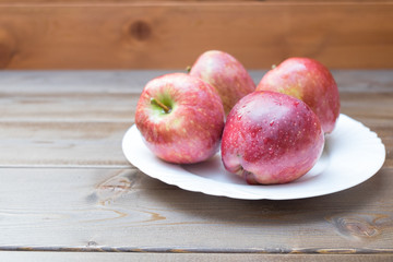 Four fresh red apples in white plate on wooden background