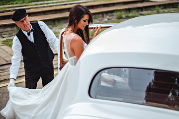 Bride entering classic car and driver holding dress