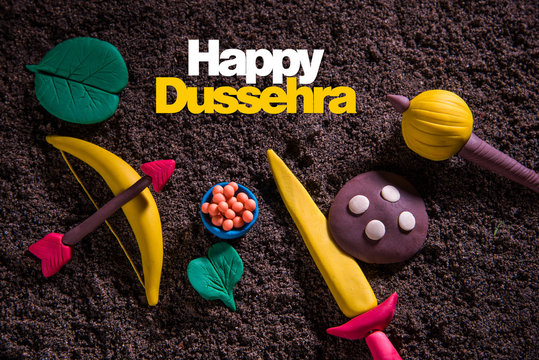 happy dussehra greeting card made using a photograph of colourful clay models of ancient indian armour used in Ramayana and Mahabharata like bow and arrow, sword and shield, gada or gadda, apta leaf
