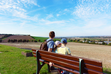 Happy family sitting on bench at meadow at summer day