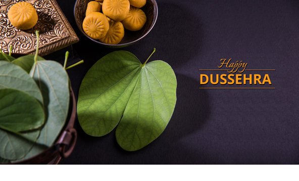 greeting card saying happy vijayadashmi or happy dussehra, indian festival dussehra, showing apta leaf or Bauhinia racemosa with traditional indian sweets pedha in silver bowl