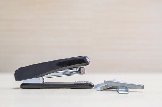 Closeup black stapler with staples  , office equipment on blurred wood desk and wall in office room textured background under window light