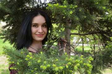 Naklejka na ściany i meble brunette girl with long hair on a background of green pine branches in the forest, long beautiful hair, natural beauty