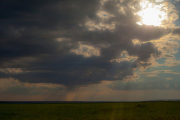 Naklejka na ściany i meble through the sky among dark gray clouds punched the sun's rays and lay down on the field