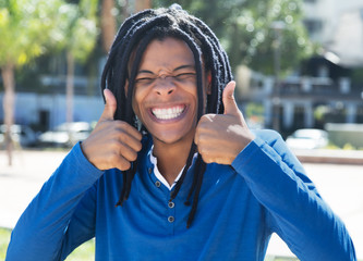 Young guy with dreadlocks showing both thumbs in the city
