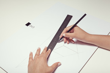 female hand drawing a cube with pen and ruler in two point perspective