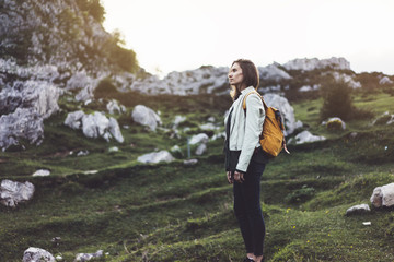 Naklejka na ściany i meble Hipster young girl with bright backpack sunset on peak of foggy mountain. Tourist traveler on background valley landscape view mockup. Hiker looking sunlight flare in trip Picos de Europa rock