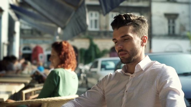 Man finsih reading menu and looking thoughtful while sitting in the outdoor cafe
