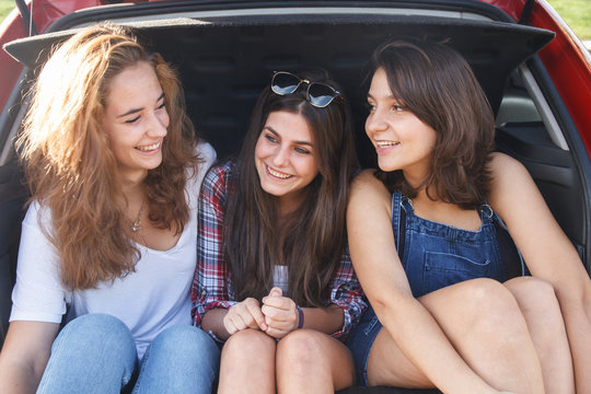 Friends having a good time and enjoying the back of the car. They are happy because they are going on vacation. The girls are smiling and laughing.  