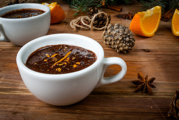 Hot chocolate with spices, orange and orange zest. Against the background of Christmas tree branches, cones and orange. Wooden table