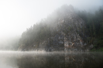 Rocky mountain in the morning fog with reflection in the river