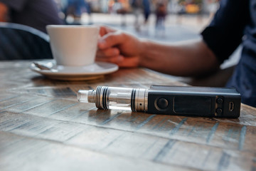 man using vape or electronic cigarette and drinking coffee