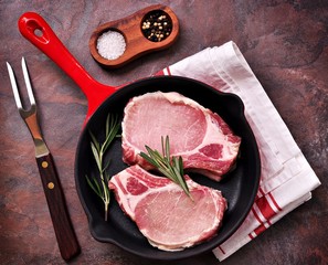 Raw pork chop in a frying pan with rosemary, pepper and salt.