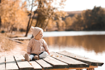 Stylish baby girl 1 year old wearing knitted autumn clothes sitting in park. Looking away. Childhood.