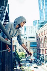 Conceptual art portrait of beautiful handsome pensive sad tired gothic young middle east brunette man with beard in hoodie, standing on staircase in city urban looking down on street