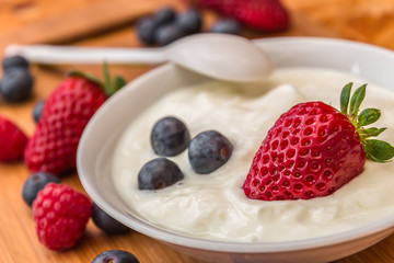 strawberries and blueberries, some of in yogurt and on wooden tr