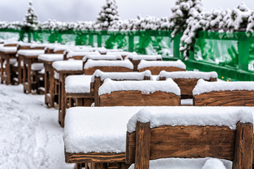 Fototapeta na wymiar Perspective row of vacant snowy wooden cafe tables at winter