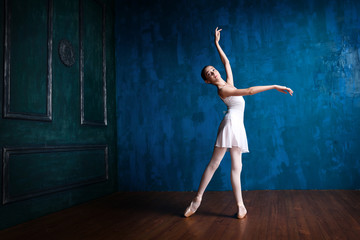 Fototapeta na wymiar Young teenage ballerina is dancing and posing in the photostudio with blue walls