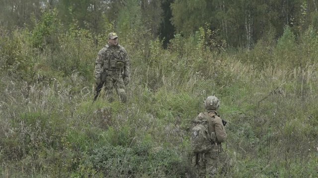Two military standing in the field and talk with a gun in his hand