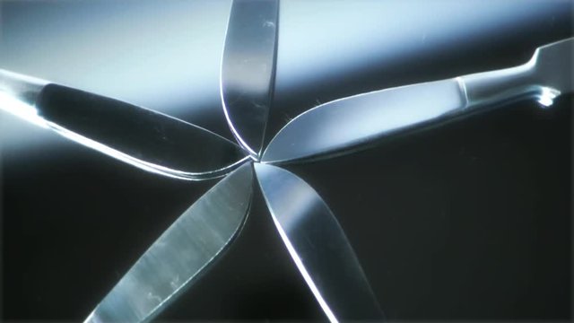 Five scalpels fanned out rotating counterclockwise on a glass mirror