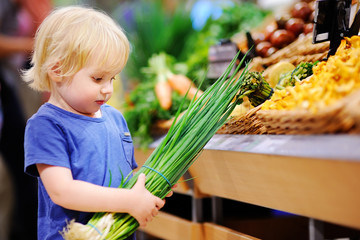 Cute toddler boy in a food store choosing fresh organic green onion