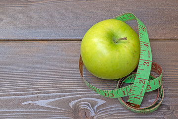 Green apple with measuring tape on wooden table