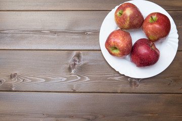 Four fresh red apples in white plate on wooden background