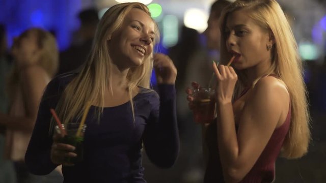 Seductive hot ladies drinking cocktails, moving sexy bodies to music at disco