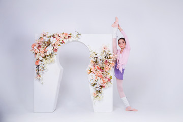 Young teenage ballerina is dancing and posing in the photostudio with white walls and white arch
