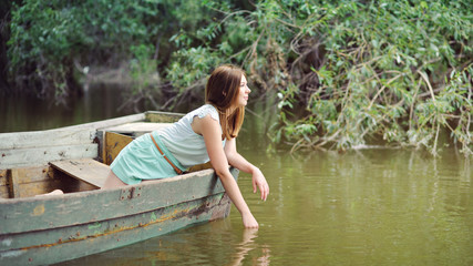 A young woman in a wooden boat floating on the river, turquoise clothing, panorama, place for text.