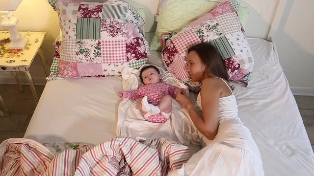 Young mother playing with her little baby on the bed - indoors