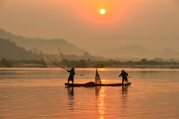 The silluate fisherman casting a net into the water on during sunrise,Thailand
