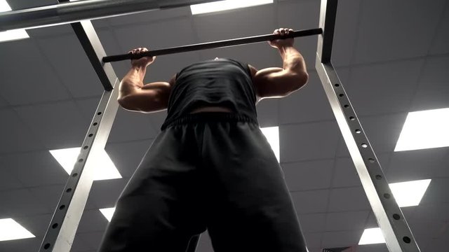 Bottom view of an athlete who is engaged in sport on the bar in the gym