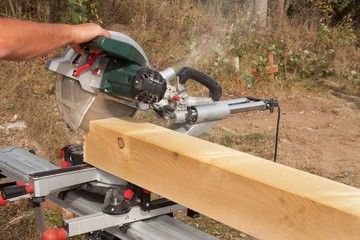 Construction Worker Cutting Beam with saw. Workers cutting timber wood with chainsaw. Saw sawing timber.

