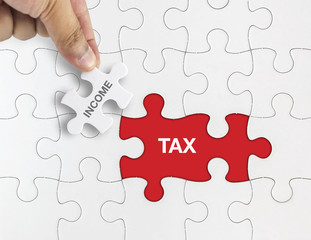 Hand holding piece of jigsaw puzzle with word INCOME TAX