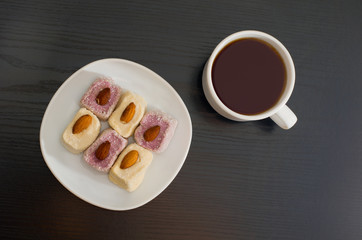 Mug of tea and Turkish Delight with almonds on a plate, top view, black background