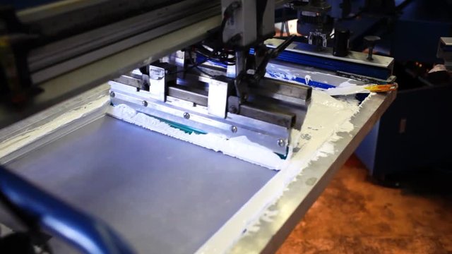 An industrial silkscreening press machine in a factory.